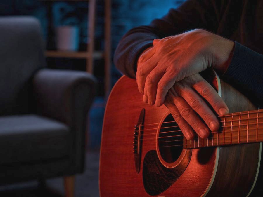 Hände ruhen sanft auf den Saiten einer Akustikgitarre in einem Therapieraum